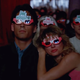A man and a woman sit in a movie theater wearing colorful 3D glasses that say "Mosquito" on them.